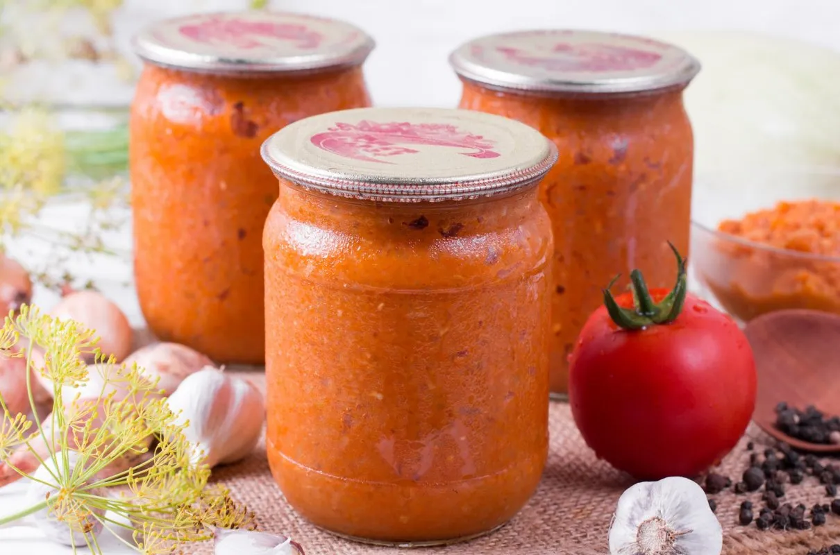 Słoiki z domowym sosem pomidorowym, idealnym do spaghetti. Obok świeże pomidory, czosnek i przyprawy.