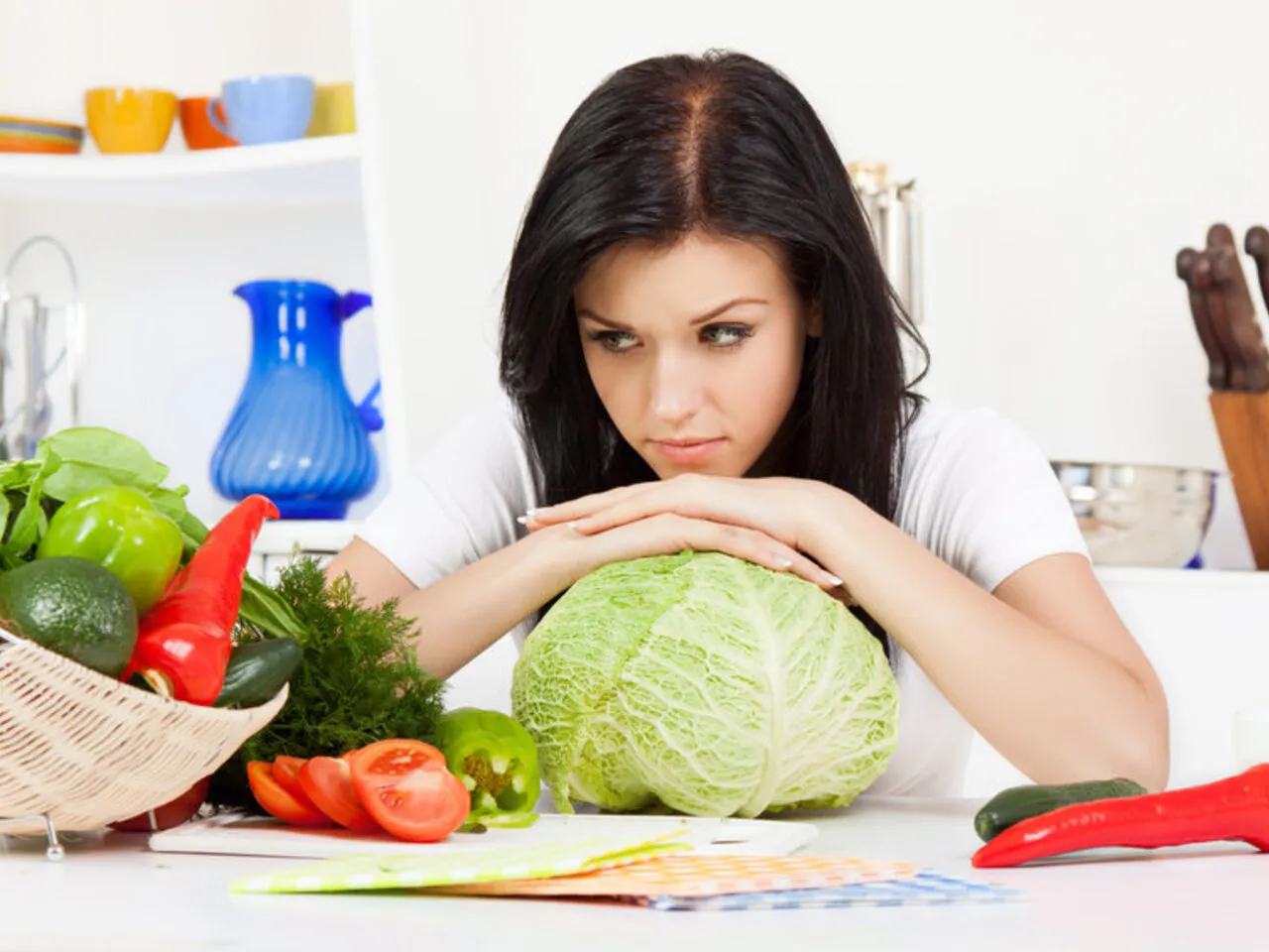 Młoda kobieta zamyślona nad kapustą, obok koszyk warzyw. Czy to początek diety kapuścianej - przepis na 7 dni?