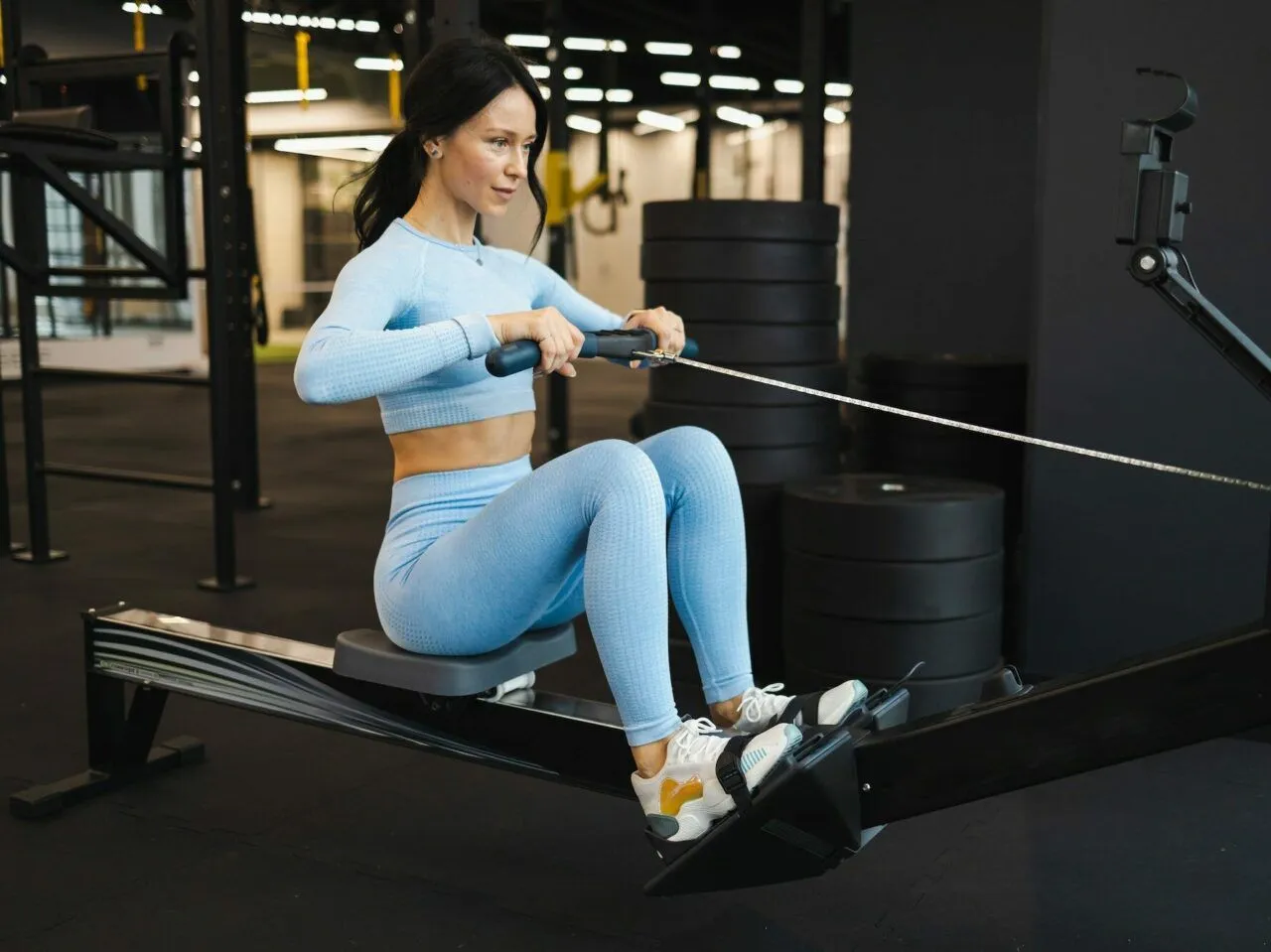 Kobieta ćwiczy na wioślarzu, pokazując, jak ćwiczyć na wioślarzu żeby schudnąć. Intensywny trening w siłowni.