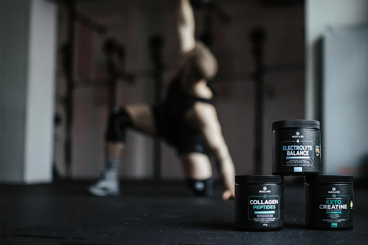 Trzy odżywki: Electrolyte Balance, Collagen Peptides i Keto Creatine, idealne jako jakie odżywki na crossfit. W tle ćwiczący sportowiec.