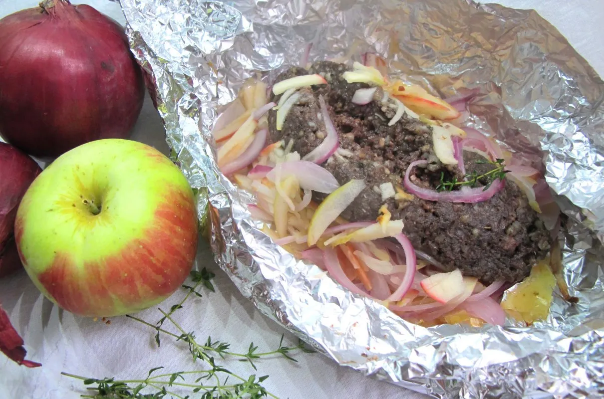 Kaszanka pieczona w folii z jabłkiem i cebulą, obok leżą świeże składniki.