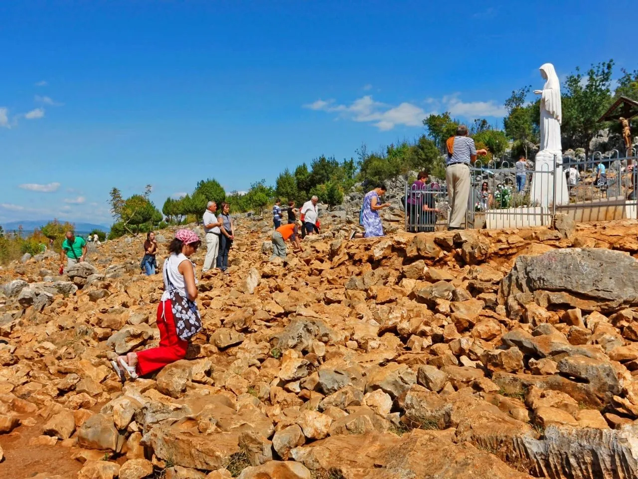 Pielgrzymi na skalistym wzg&oacute;rzu w Medziugorie. Wiele os&oacute;b klęczy, modląc się. Czy w Medziugorie jest bezpiecznie? Tak, to miejsce pielgrzymek.