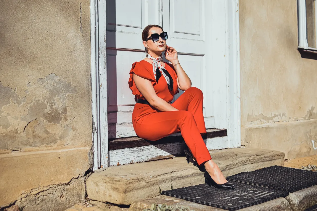 Elegancka kobieta w czerwonym kombinezonie i czarnych szpilkach. Idealne buty do czerwonego kombinezonu to klasyczne czarne cz&oacute;łenka.