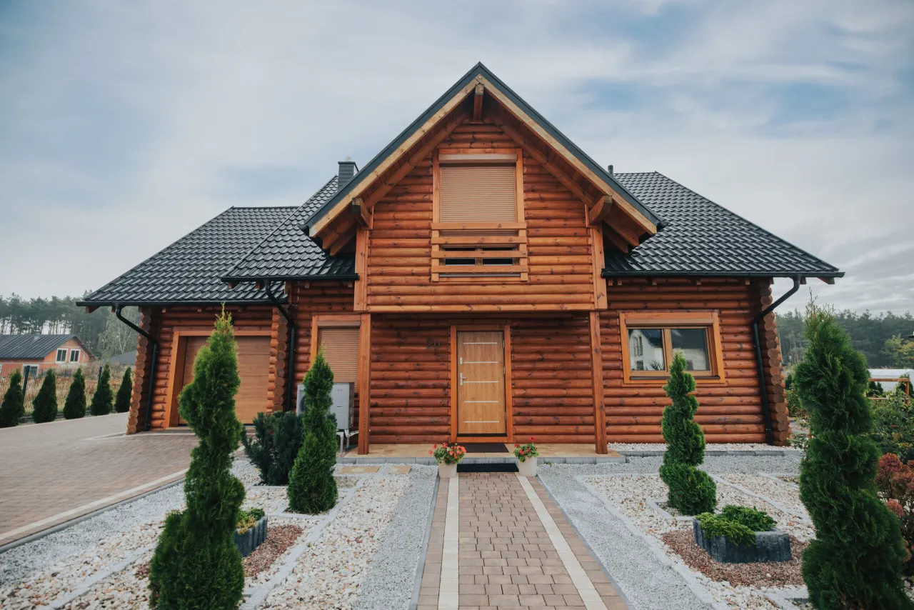 Piękny drewniany dom z bali, z czarnym dachem i zadbanym ogrodem. Zastanawiasz się, ile kosztuje budowa domu drewnianego 100m2?