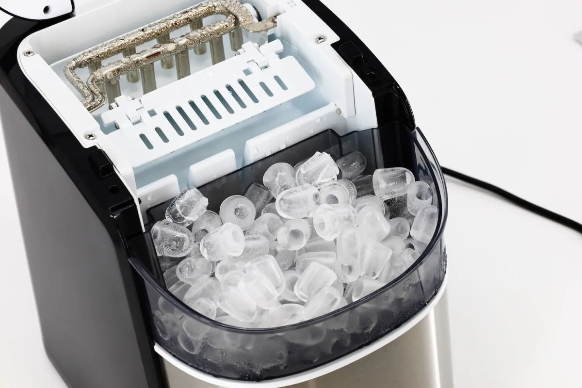 Wnętrze kruszarki do lodu z pełnym pojemnikiem lodowych kostek. Urządzenie gotowe do schłodzenia napojów.