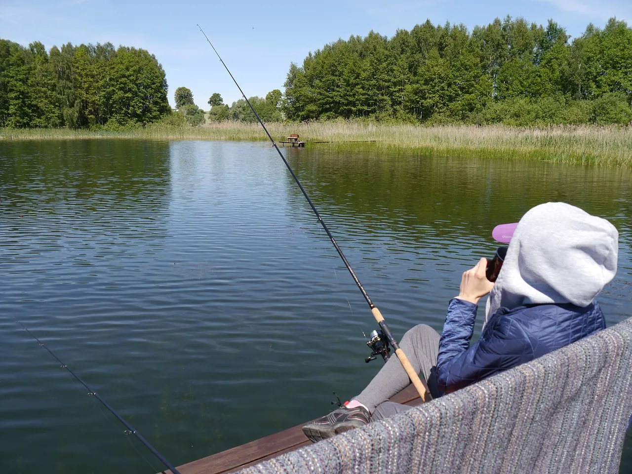 Idealne miejsce, gdzie na ryby na Mazury. Spokojna tafla jeziora, zielone lasy i wędkarz czekający na branie.