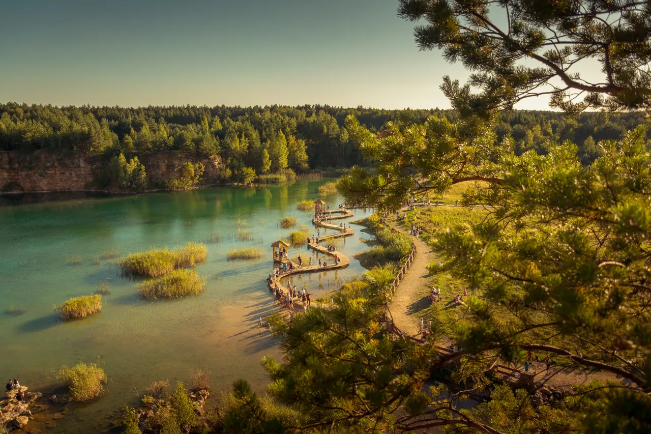 Malowniczy rezerwat przyrody Dolina Żabnika z drewnianymi kładkami wśr&oacute;d turkusowej wody i zieleni.