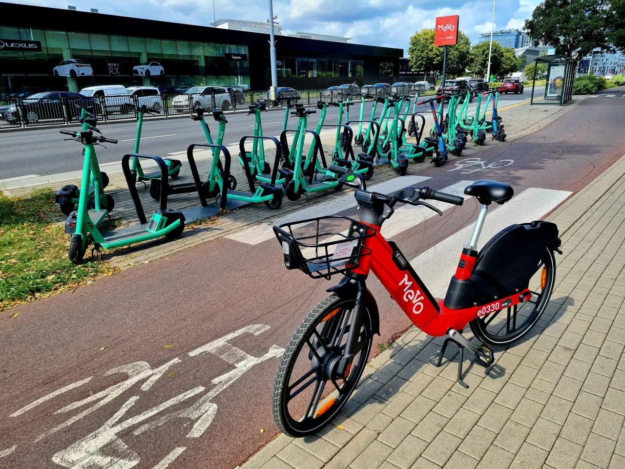Czerwony rower i zielone hulajnogi czekają na przejażdżkę po trasach rowerowych Tr&oacute;jmiasta.