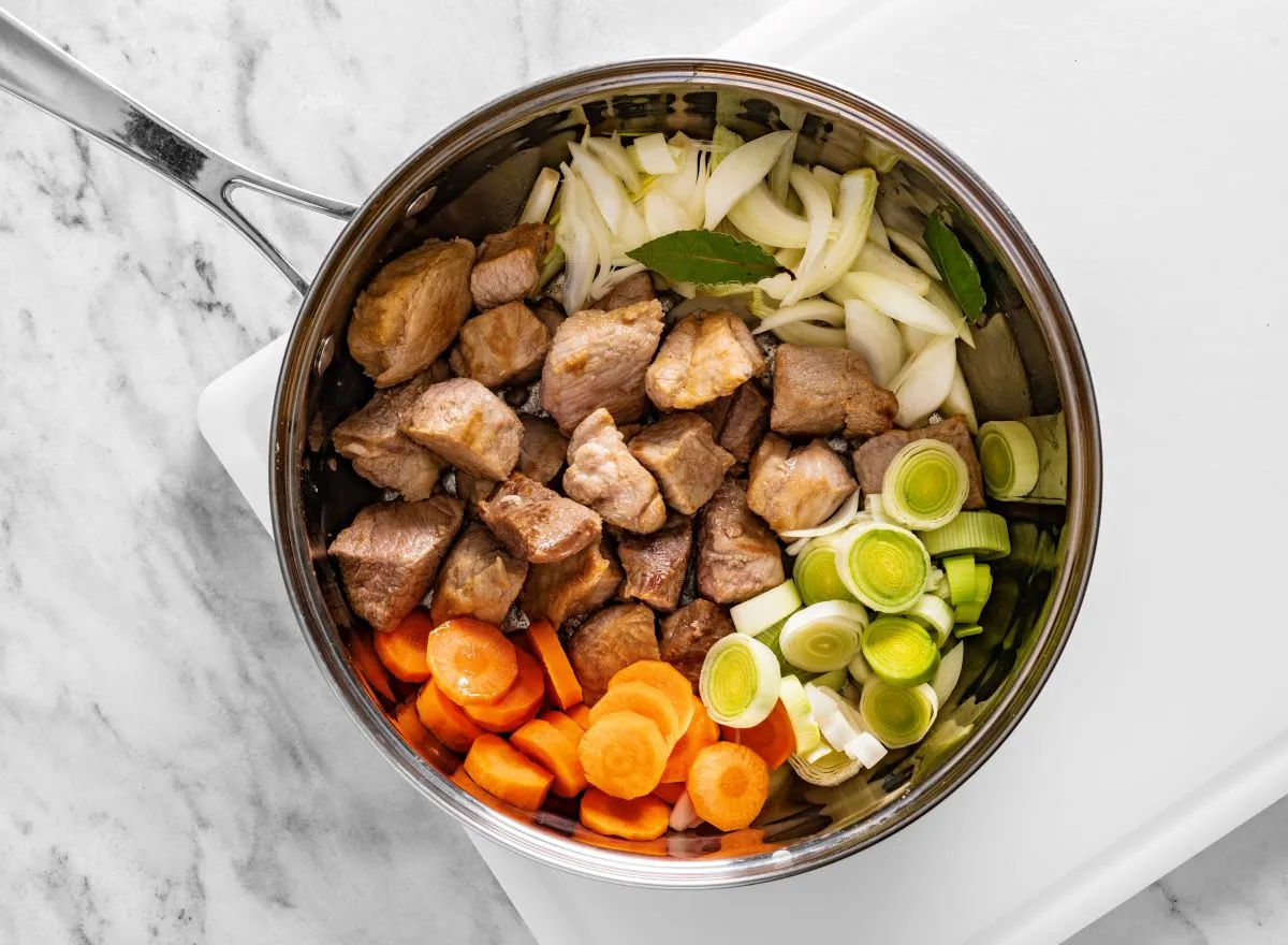 Kawałki wieprzowiny, marchewka, por, cebula i liście laurowe w garnku &ndash; składniki do sosu z mięsa wieprzowego.