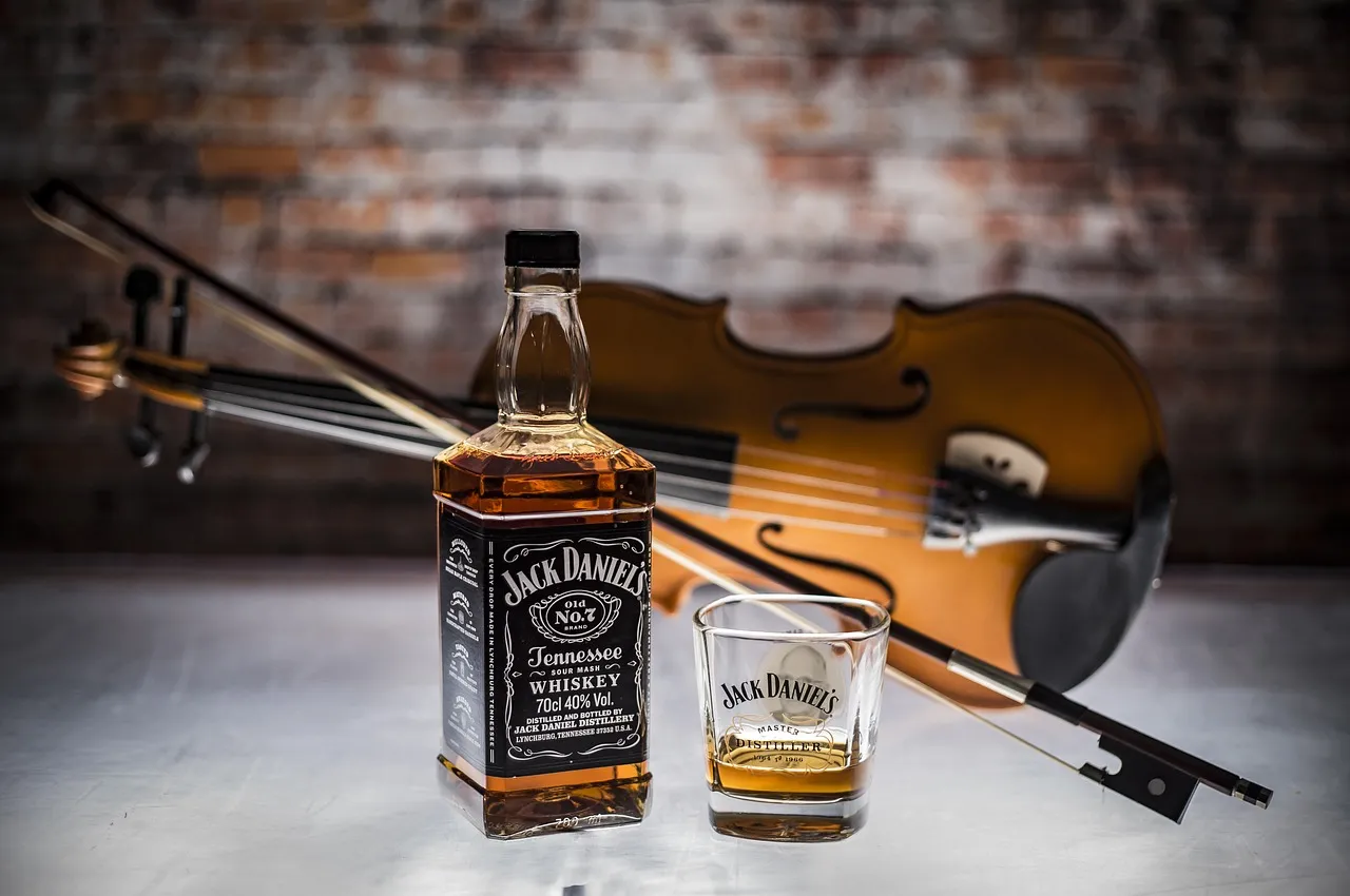 Butelka Jack Daniel's Tennessee Whiskey i kieliszek obok skrzypiec. Różnica między whisky a whiskey oraz bourbonem a scotchem jest subtelna.