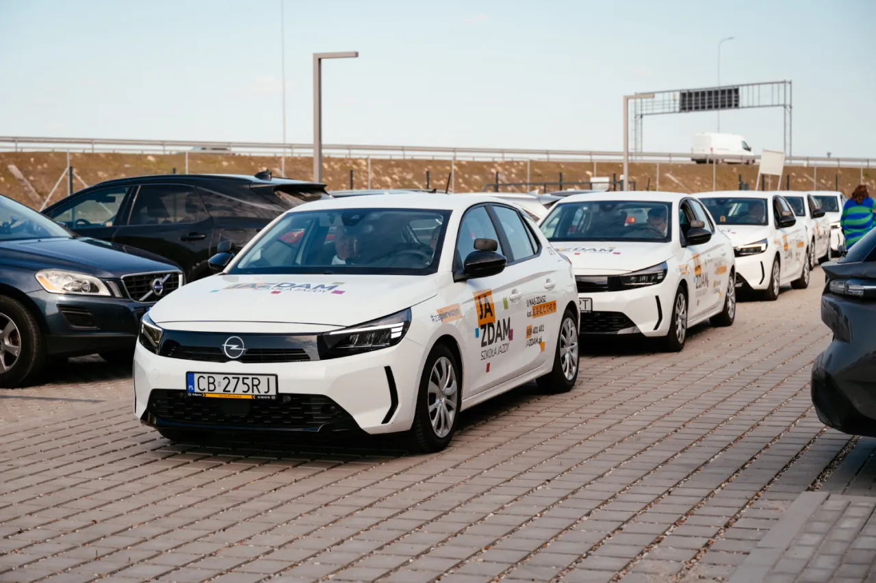Białe samochody szkoleniowe ustawione w rzędzie, gotowe do nauki jazdy. Idealne dla os&oacute;b, kt&oacute;re chcą zdobyć prawo jazdy wiek 17 lat.