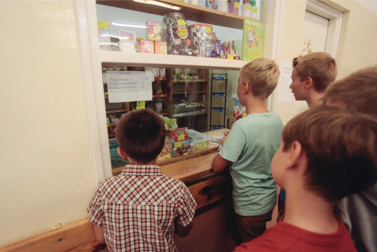 Chłopcy patrzą na cennik w sklepiku szkolnym. Można tam kupić słodycze, bułki i napoje.