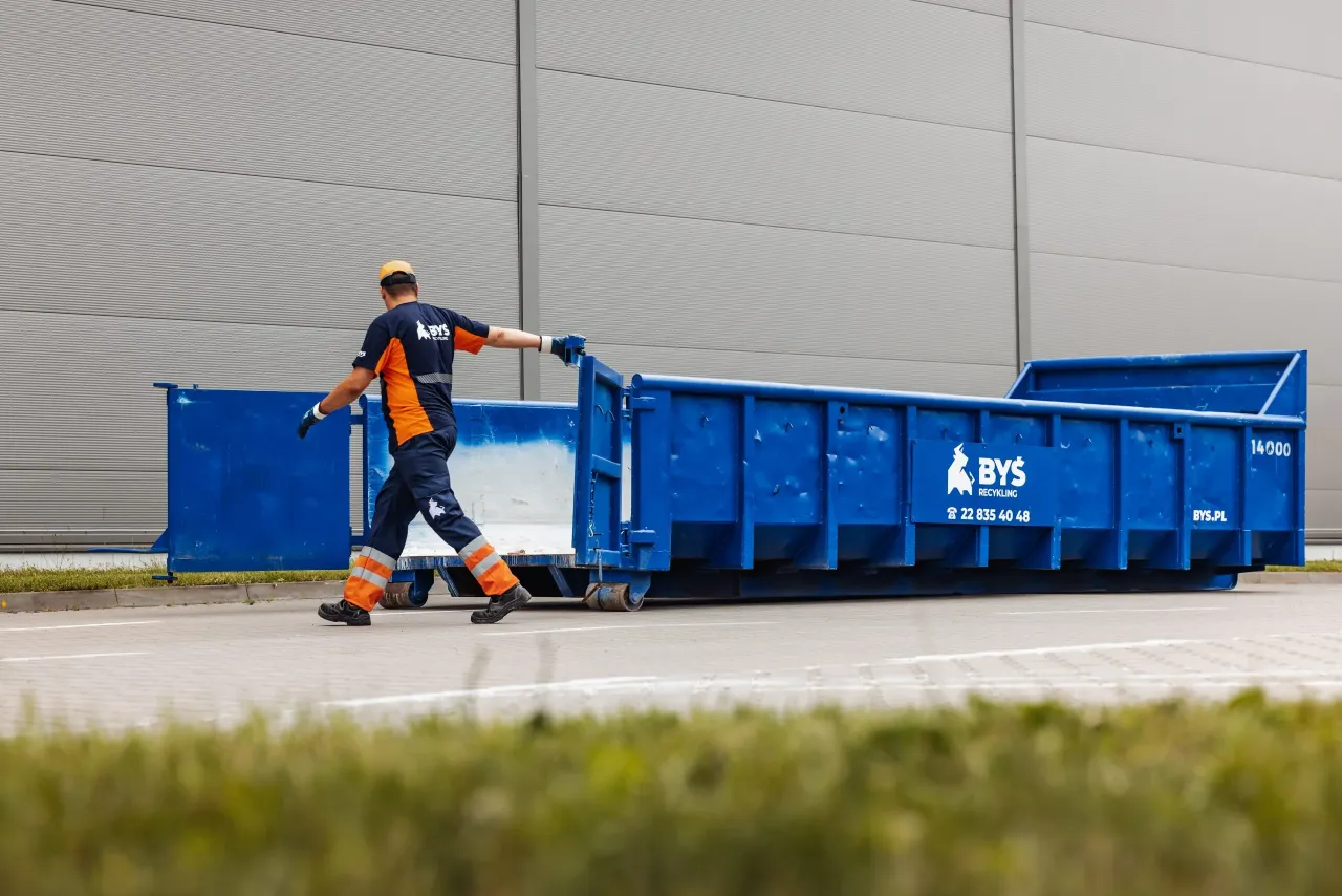 Pracownik firmy BYŚ Recycling obsługuje kontener. Zastanawiasz się, jaki vat naliczany jest przy wywozie śmieci?