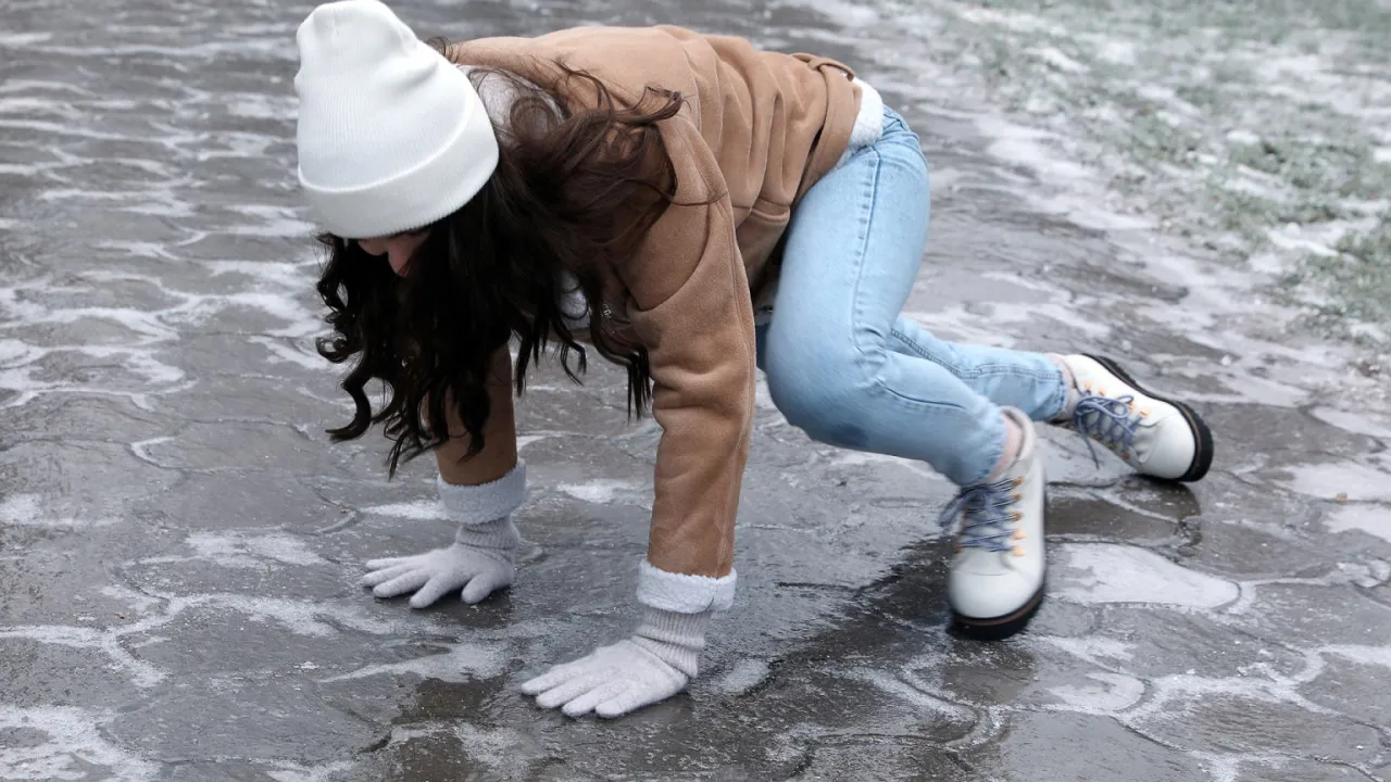 Dziewczyna na lodzie pada, pokazując, jak zabezpieczyć buty przed poślizgiem.