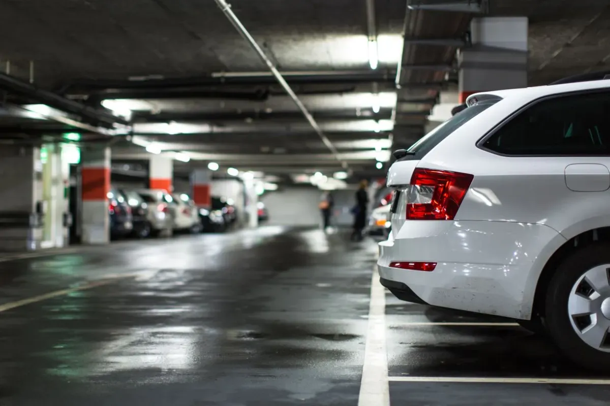 Biały samoch&oacute;d na parkingu podziemnym. Rozważasz wynajem samochodu od osoby prywatnej a podatek?