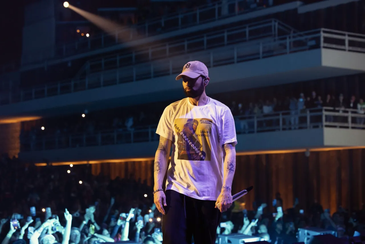 Eminem na scenie, w czapce i koszulce z nadrukiem. Fani zastanawiają się, ile zarabia Eminem, widząc jego sukces.