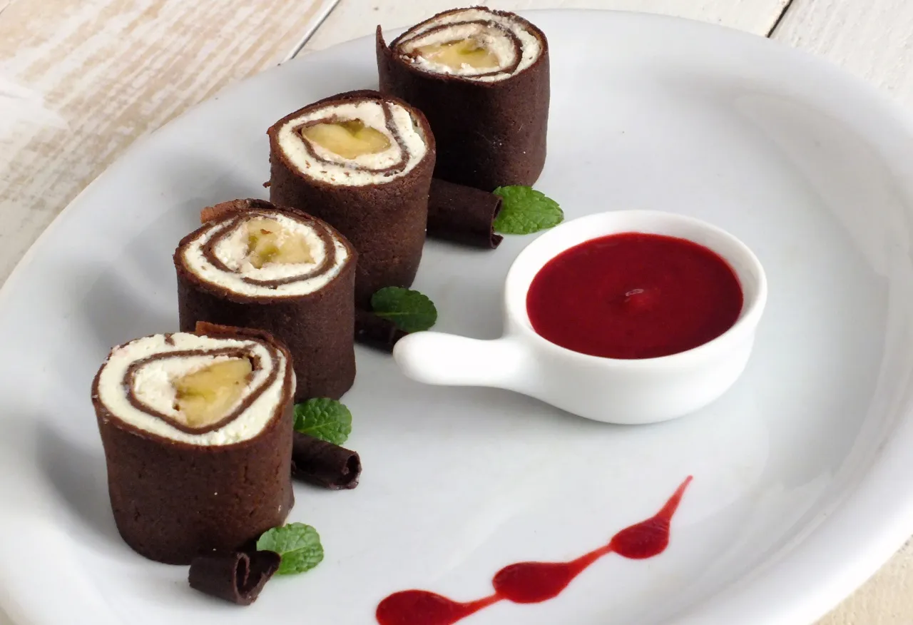 Czekoladowe rolki z bananem i kremem, podane jako sushi na słodko, z malinowym sosem i miętą.