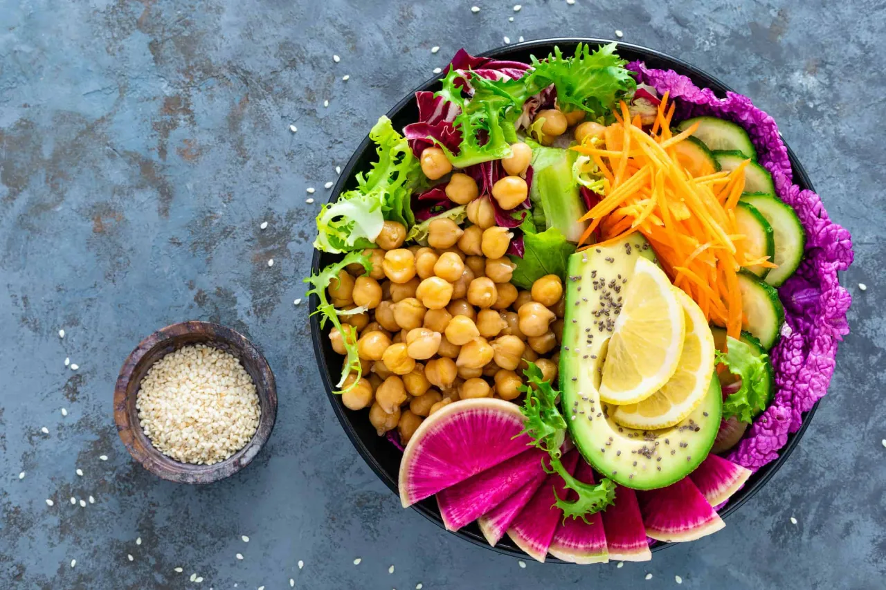 Kolorowa buddha bowl z ciecierzycą, awokado, rzodkiewką, og&oacute;rkiem, marchewką i sałatą.