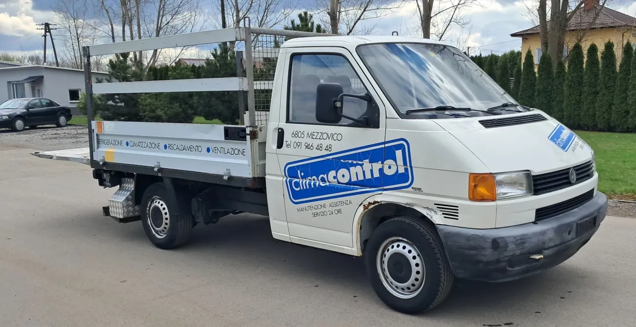 Biały Volkswagen Transporter z zabudową skrzyniową, idealny jako tani bus do 10 tys. zł. Na drzwiach logo 