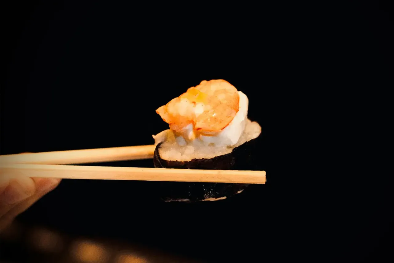 Jak trzymać pałeczki do sushi? Oto przykład z krewetką na ryżu i nori.