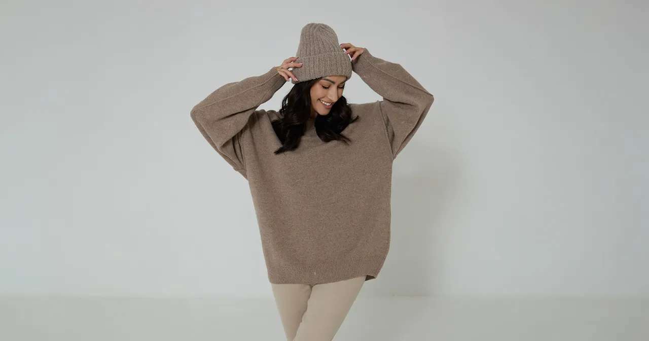 Uśmiechnięta kobieta w beżowym swetrze z szenili i czapce. Miękki sweter z szenili to idealny wyb&oacute;r na chłodne dni.