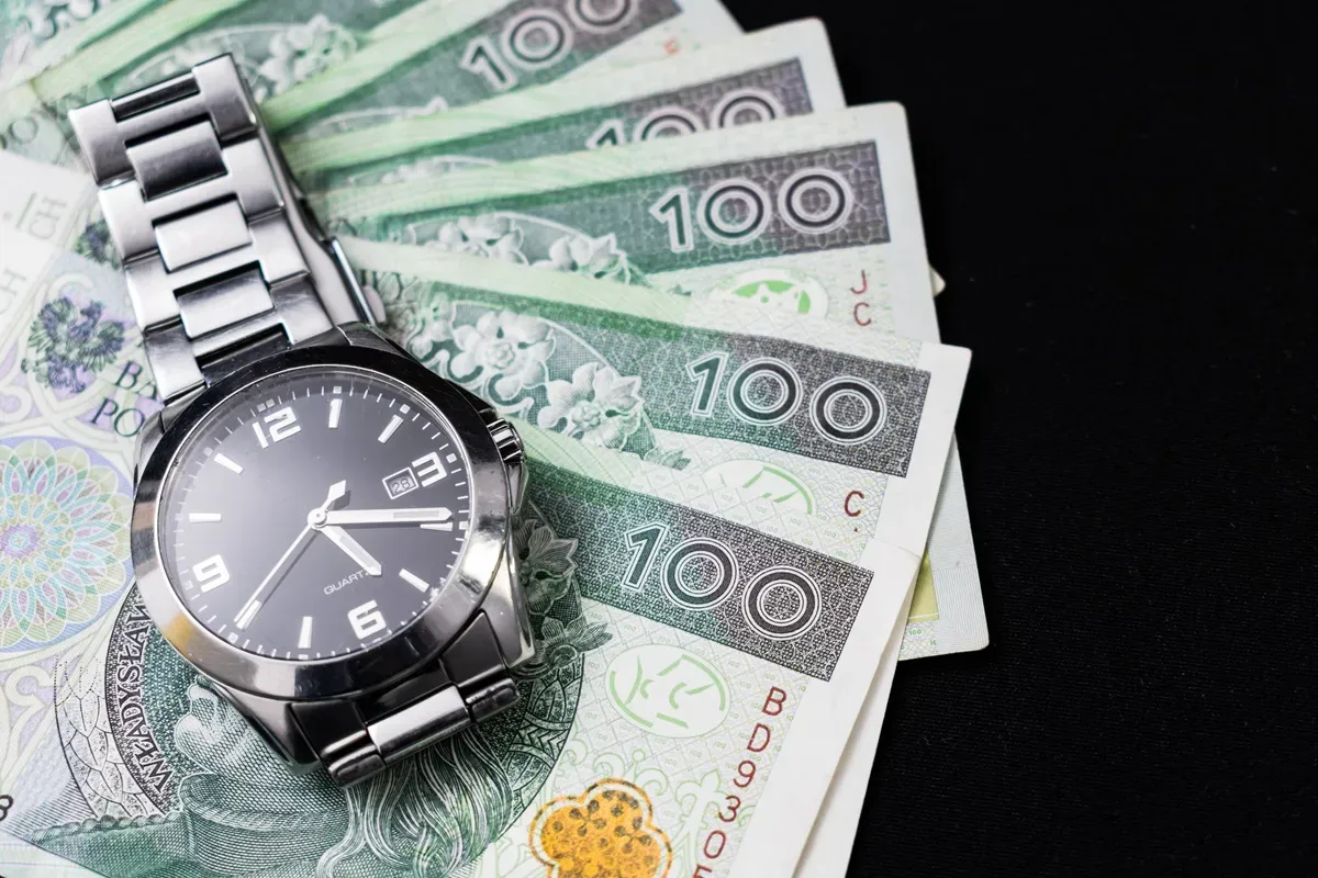 Zegarek na stosie banknot&oacute;w 100 zł. Czas to pieniądz, zwłaszcza gdy chodzi o opłacanie składek ZUS samemu.
