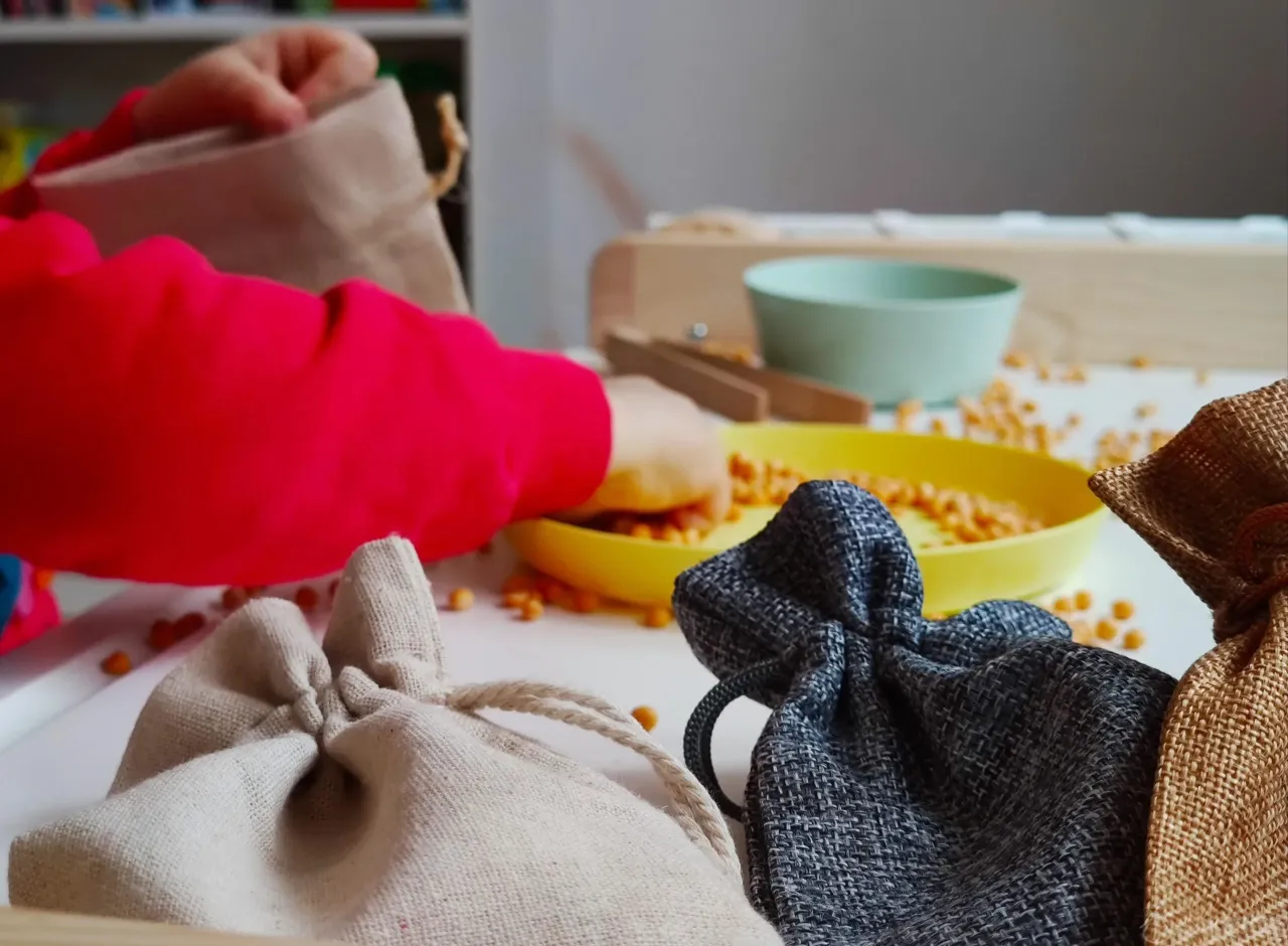 Dziecko wkłada rękę do woreczka, obok leżą inne woreczki sensoryczne DIY i rozsypana ciecierzyca.
