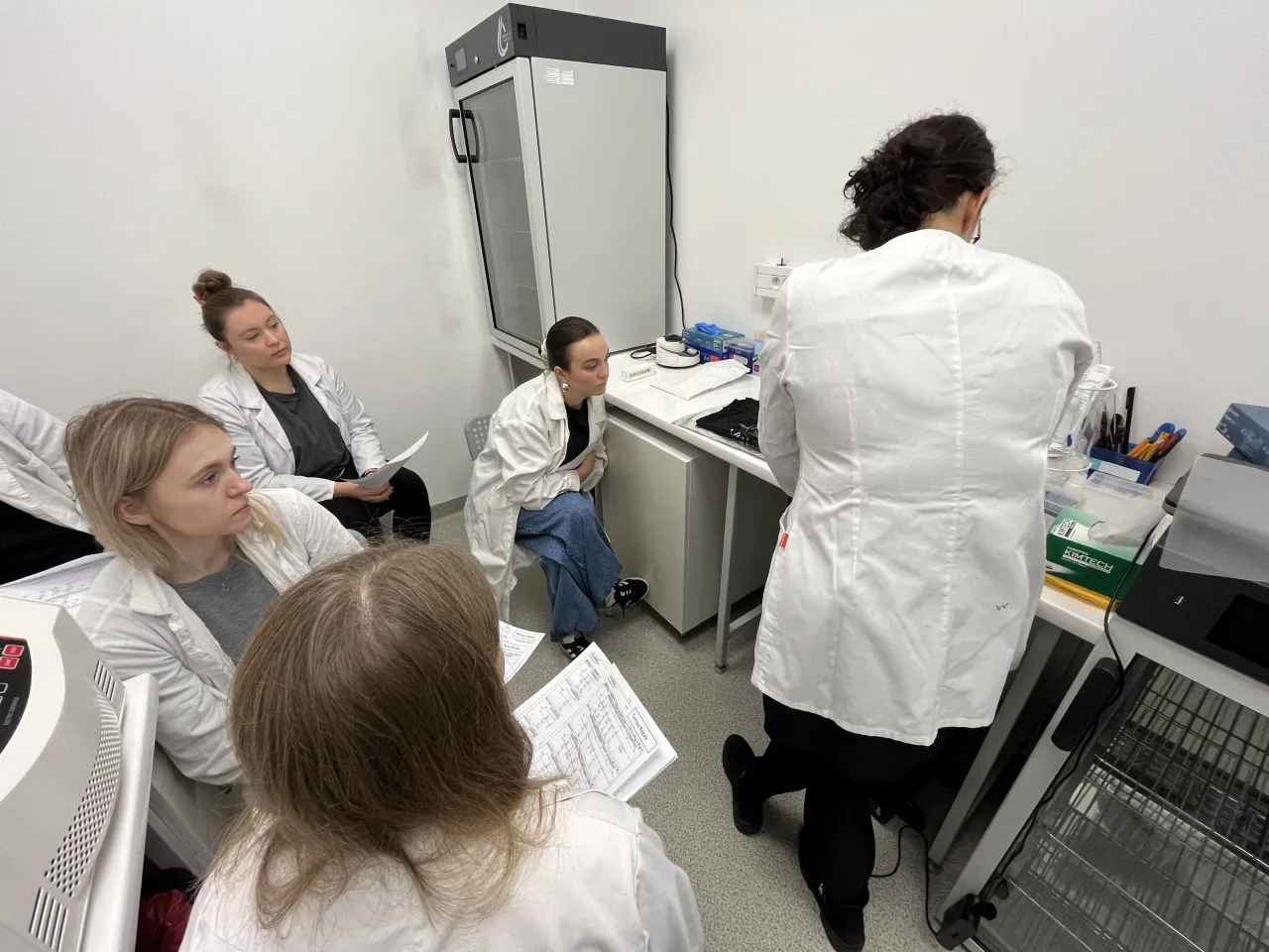 Grupa studentów w kitlach słucha wykładu w laboratorium. Czy praca w laboratorium jest trudna? Zależy od podejścia!