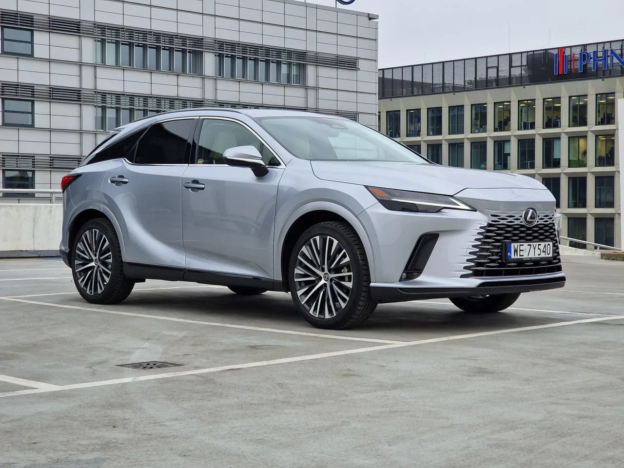 Srebrny Lexus RX na parkingu przed nowoczesnym budynkiem. Idealne auto na długie trasy, gotowe na każdą podr&oacute;ż.