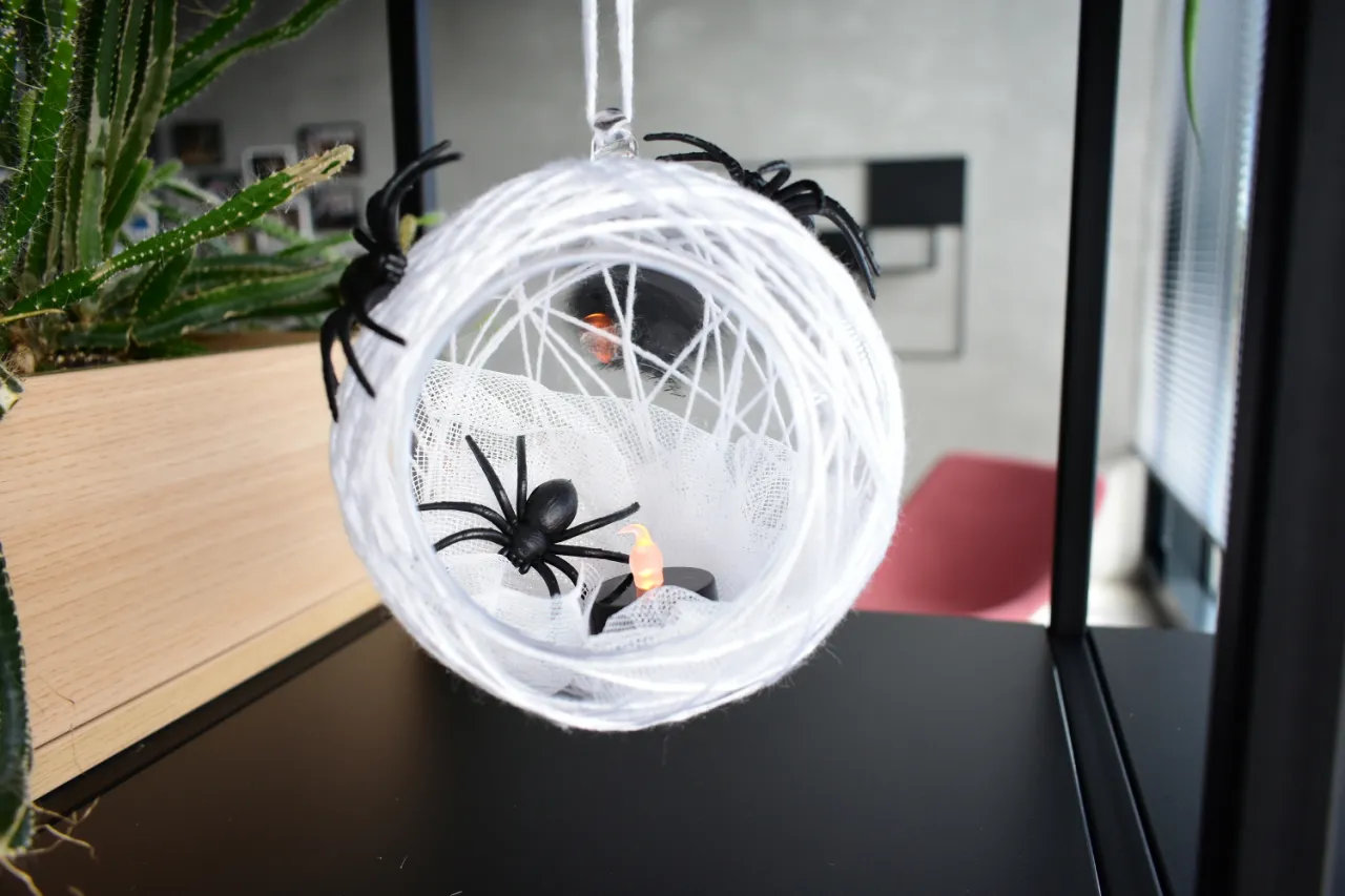 Dekoracja na Halloween: biała pajęczyna z czarnymi pająkami i świeczką.