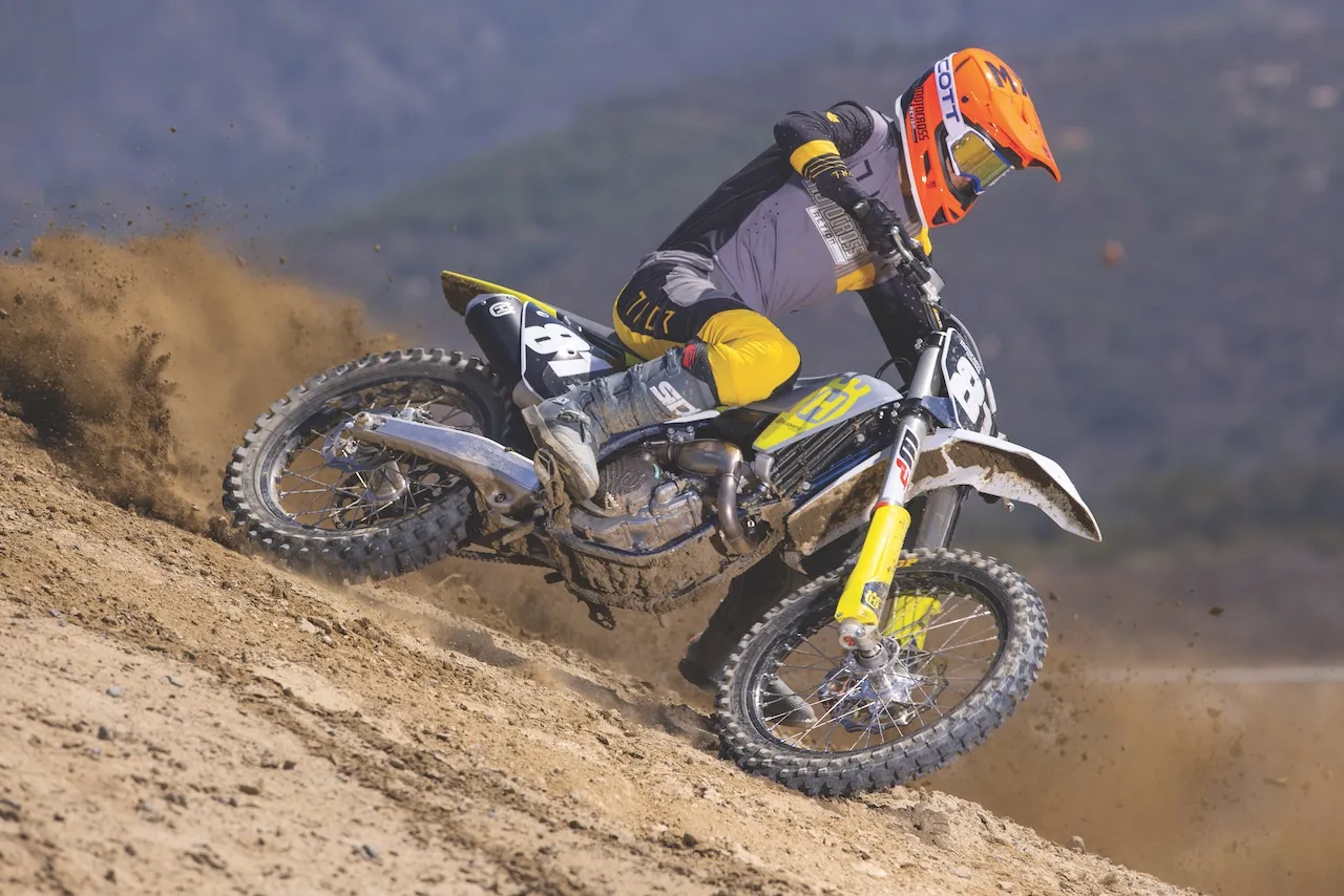 Motocyklista na Husqvarna 250 FE pokonuje zakręt na piaszczystym torze, wzbijając tumany kurzu.