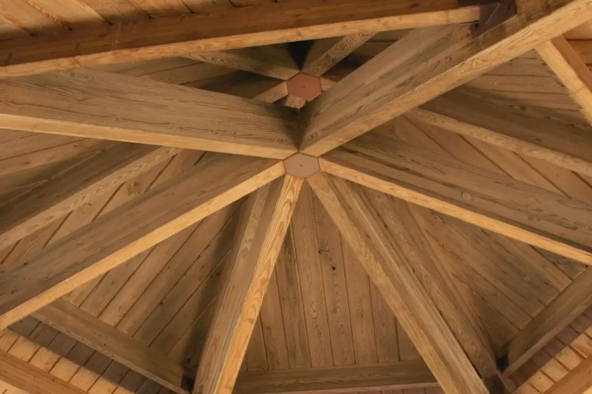 Drewniana konstrukcja dachu altany. Widoczne belki i deski tworzące solidne zadaszenie.