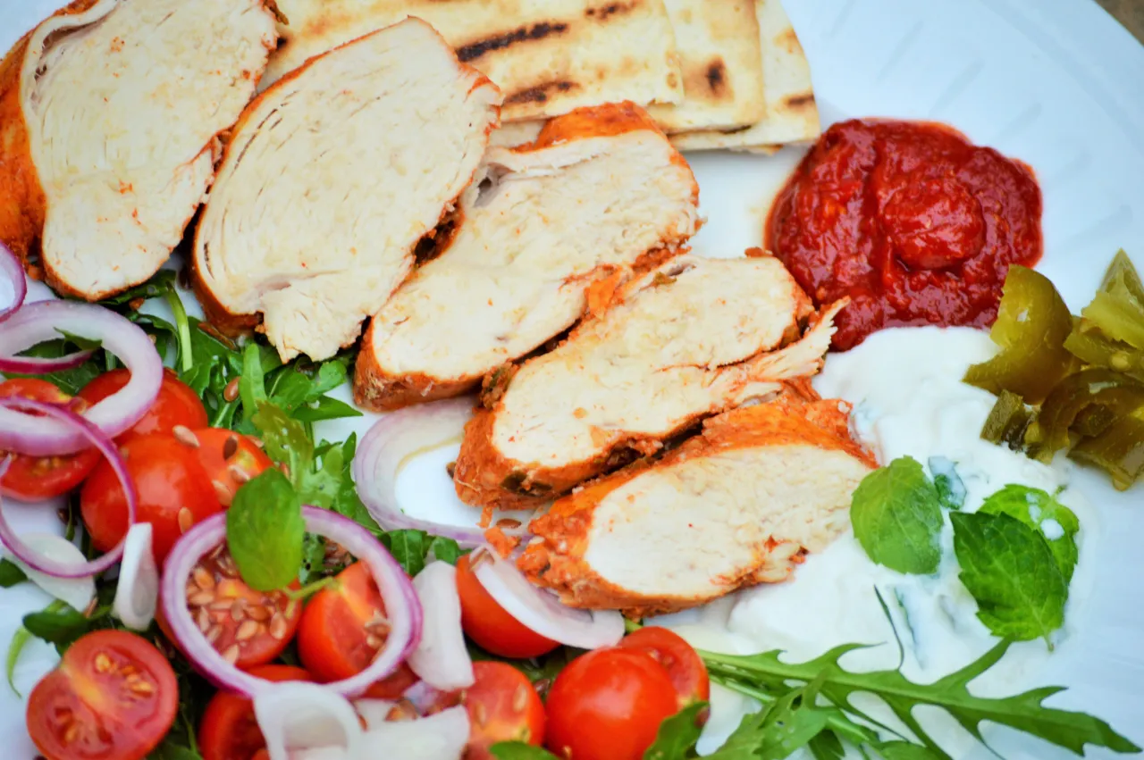 Pokrojona pierś z kurczaka pieczona bez tłuszczu, podana z warzywami, dipem i pitą. Idealna na dietetyczny obiad.