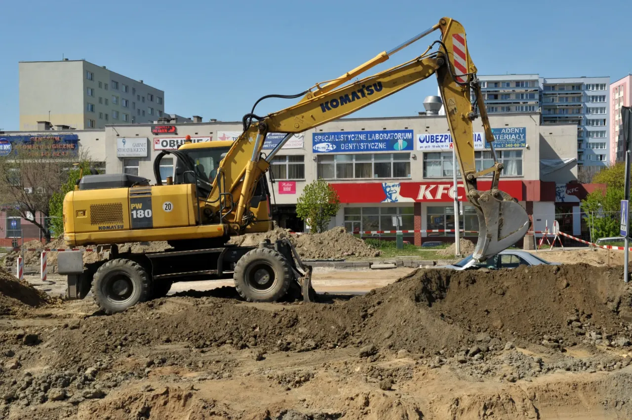 Żółta koparka Komatsu PW 180 pracuje na budowie, kopiąc dół, w którym widać samochód. Czy koparka ma dowód rejestracyjny?