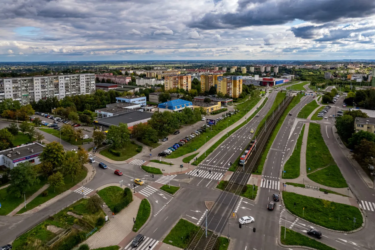 Widok z lotu ptaka na ruchliwe skrzyżowanie w Gdańsku Chełmie, z tramwajem, samochodami i budynkami mieszkalnymi w tle.