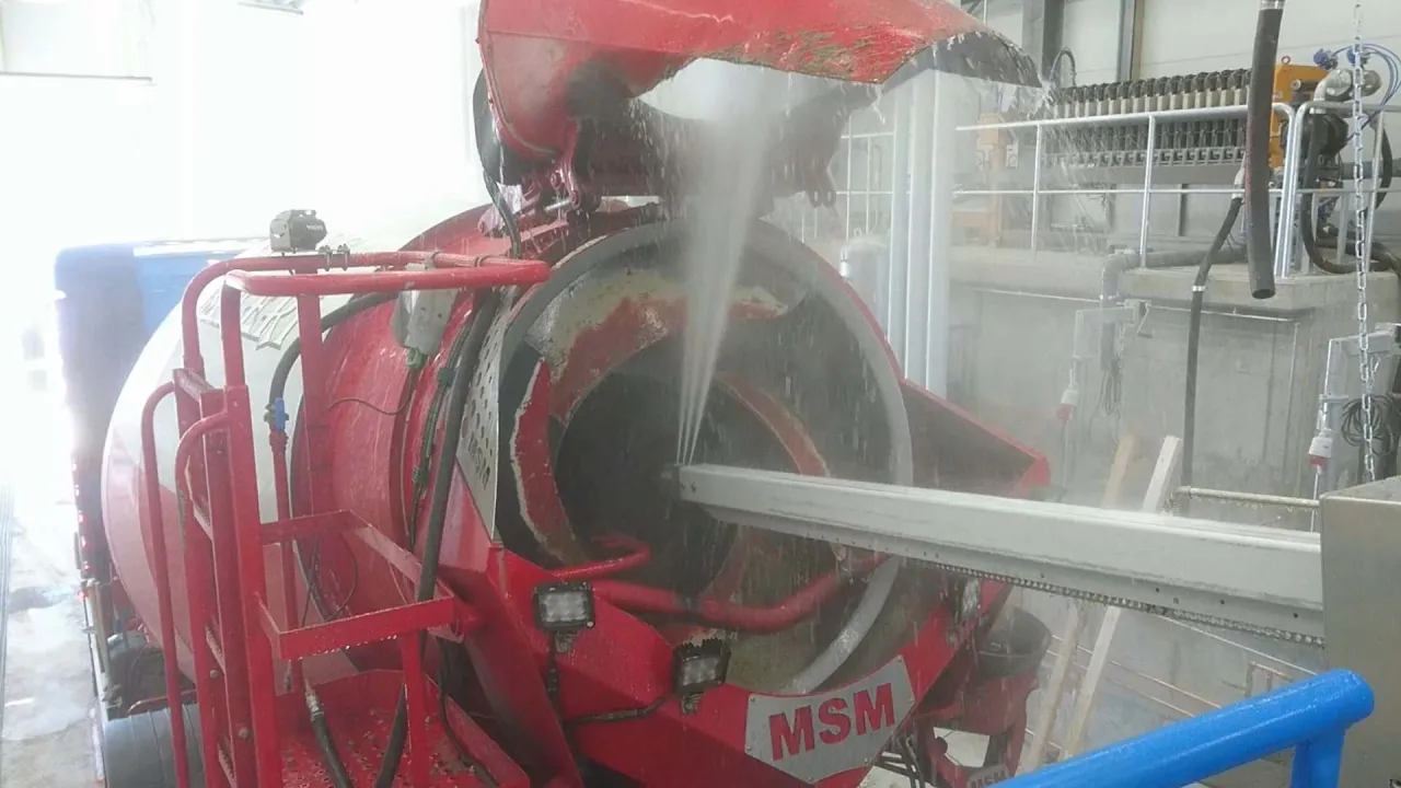 Czyszczenie betoniarki wodą pod ciśnieniem. Woda leje się do wnętrza bębna, usuwając resztki betonu.