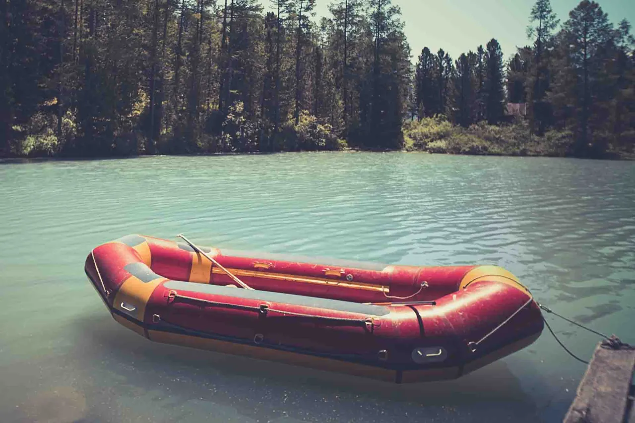 Czerwony ponton z wiosłem, idealny jako jaki ponton na ryby, unosi się na spokojnej, turkusowej wodzie, w tle las.