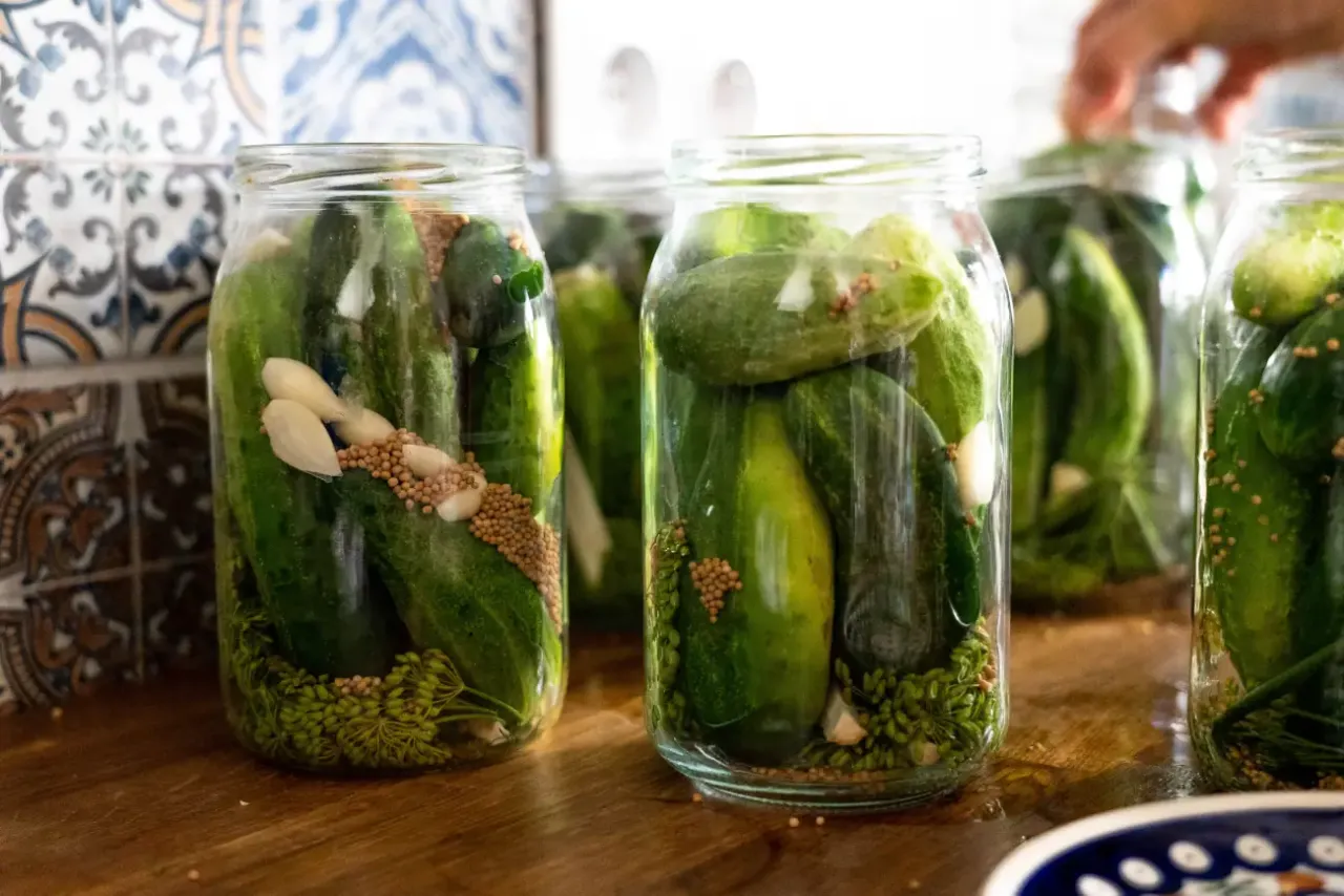 Słoiki z ogórkami, czosnkiem, koprem i gorczycą, przygotowane do pasteryzowania w piekarniku.