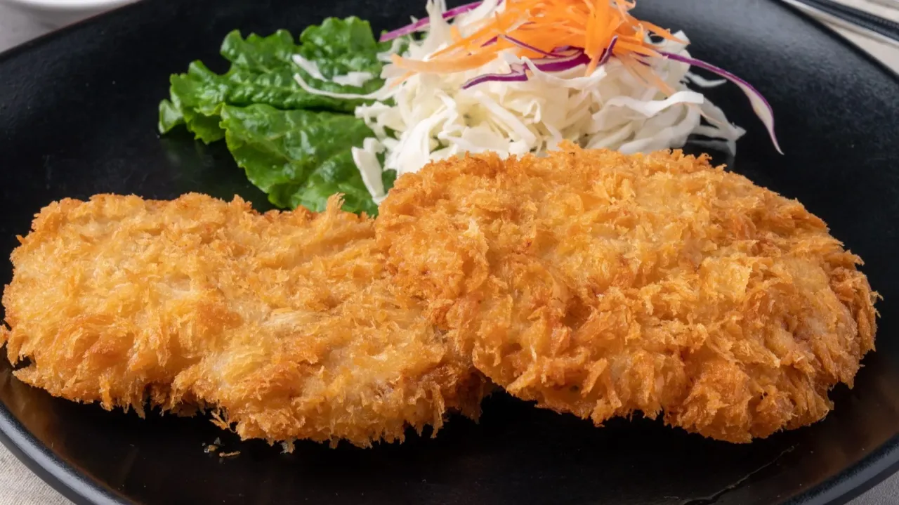 Dwa chrupiące kotlety z kurczaka w panko, podane z sałatką z kapusty i marchewki na czarnym talerzu.