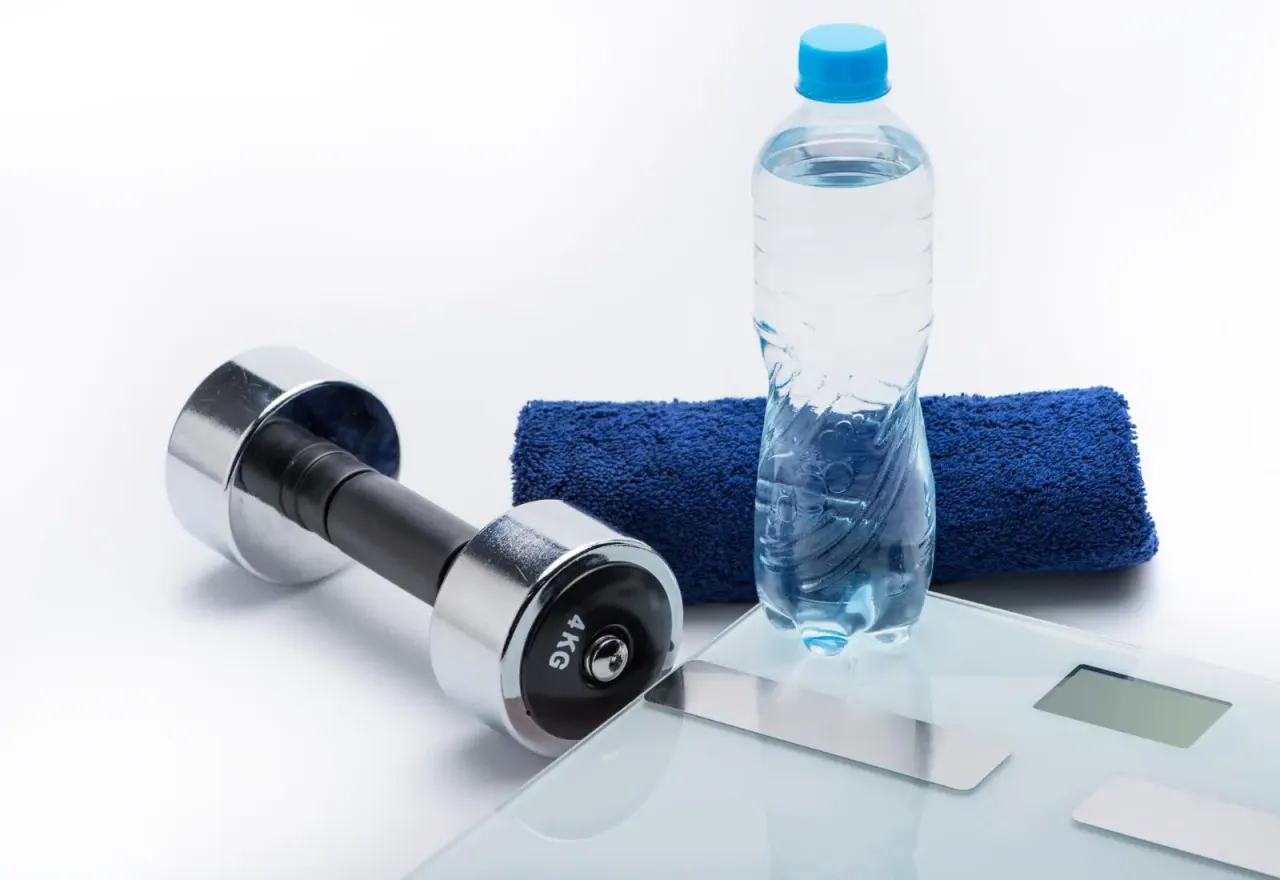 Hantle, ręcznik, butelka wody i waga. Pytanie: czy kreatynę trzeba rozpuszczać w wodzie?