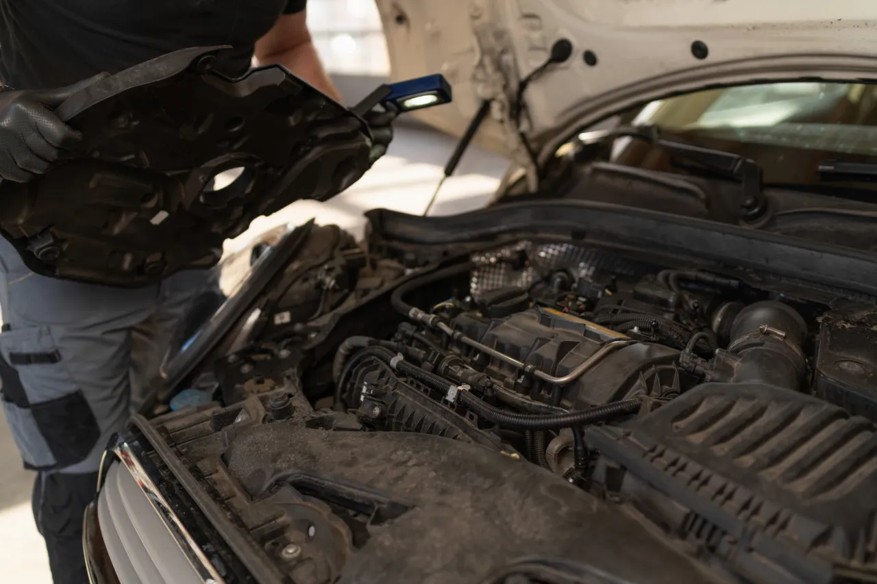 Mechanik sprawdza silnik, szukając objaw&oacute;w przegrzania. Widać elementy silnika i narzędzia.