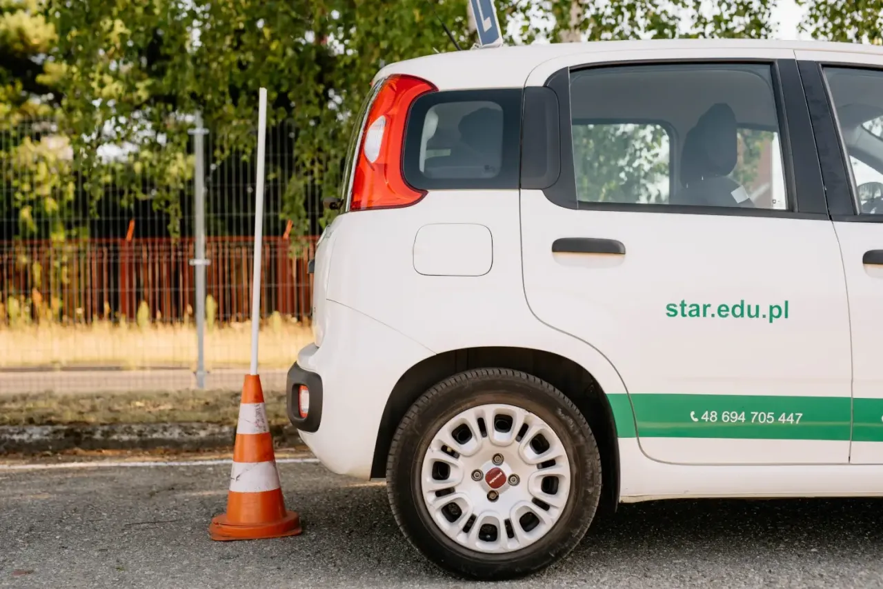Biały samoch&oacute;d szkoleniowy z pachołkiem obok. Zastanawiasz się, ile kosztuje prawo jazdy? Sprawdź ofertę na star.edu.pl.