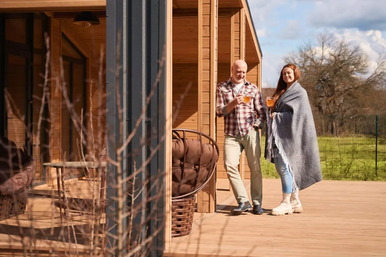 Para, jak dostać dofinansowanie na domki letniskowe, rozmawiają na tarasie swojego nowego, drewnianego domu.