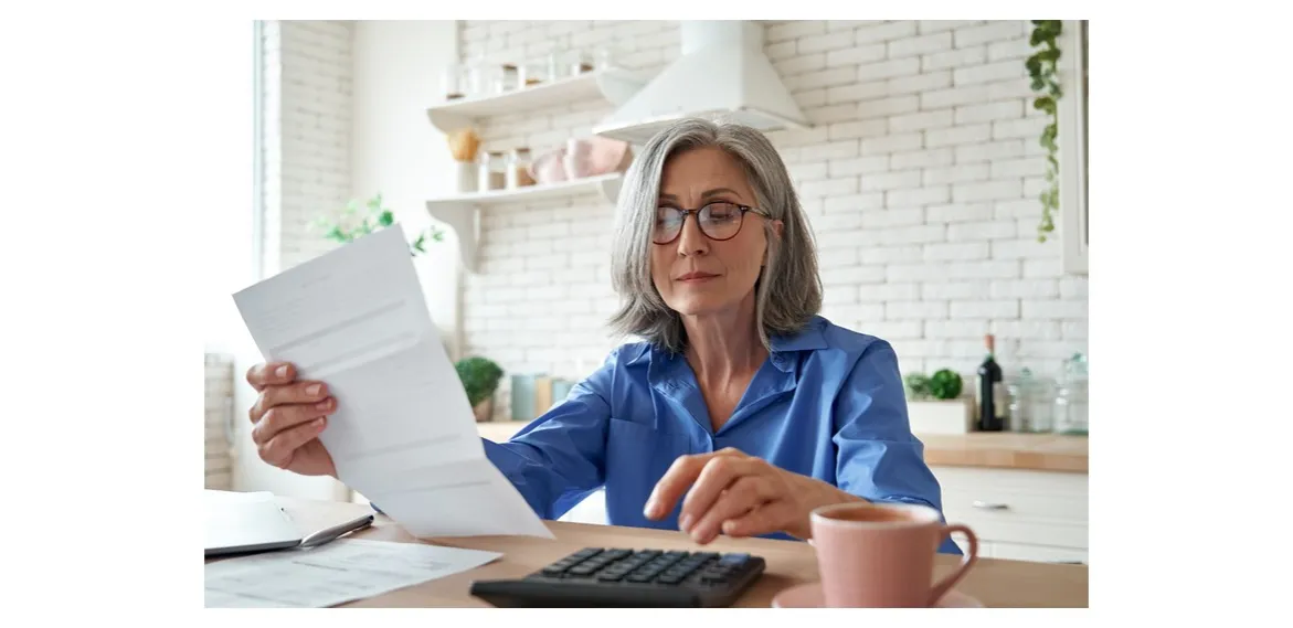 Kobieta po 50. roku życia analizująca budżet domowy, z kalkulatorem i notatkami