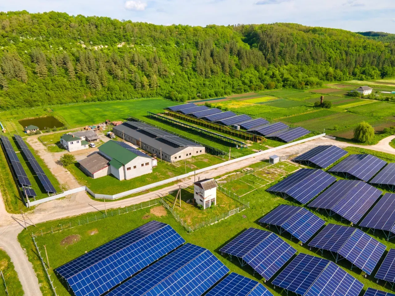 Duża farma fotowoltaiczna, gdzie panele oze rentier czerpią energię ze słońca, otoczona zielonymi wzg&oacute;rzami i polami.