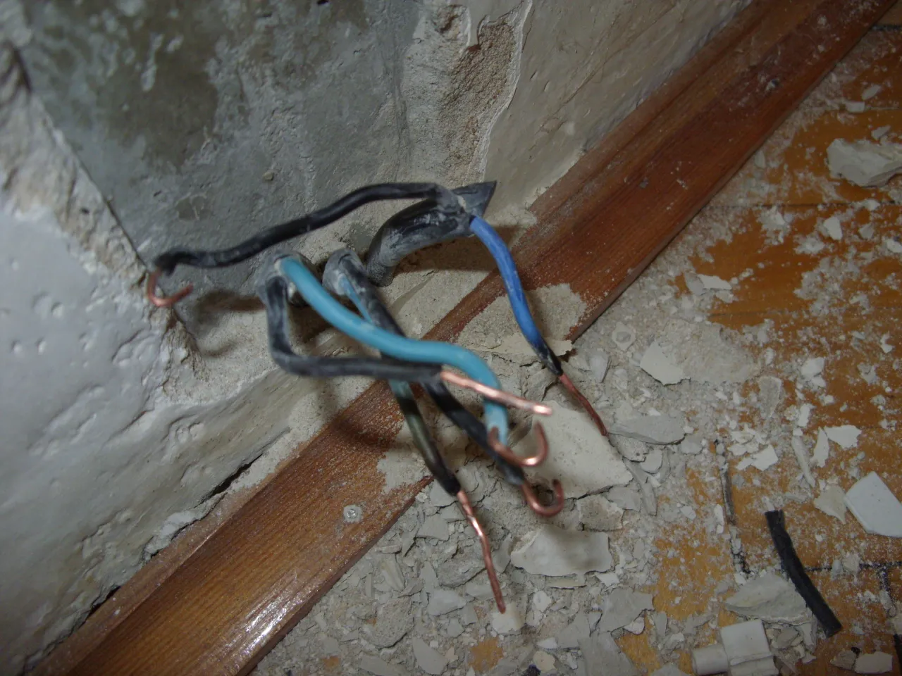 Luźne przewody elektryczne, w tym niebieski przewód neutralny, wystają z betonowej ściany. Widać odsłonięte miedziane końcówki, co może oznaczać małe napięcie na przewodzie neutralnym.