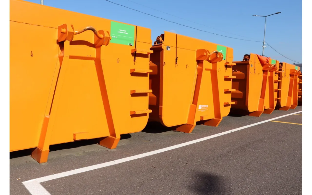 Rzędy pomarańczowych kontenerów na śmieci w Warszawie czekają na załadunek.