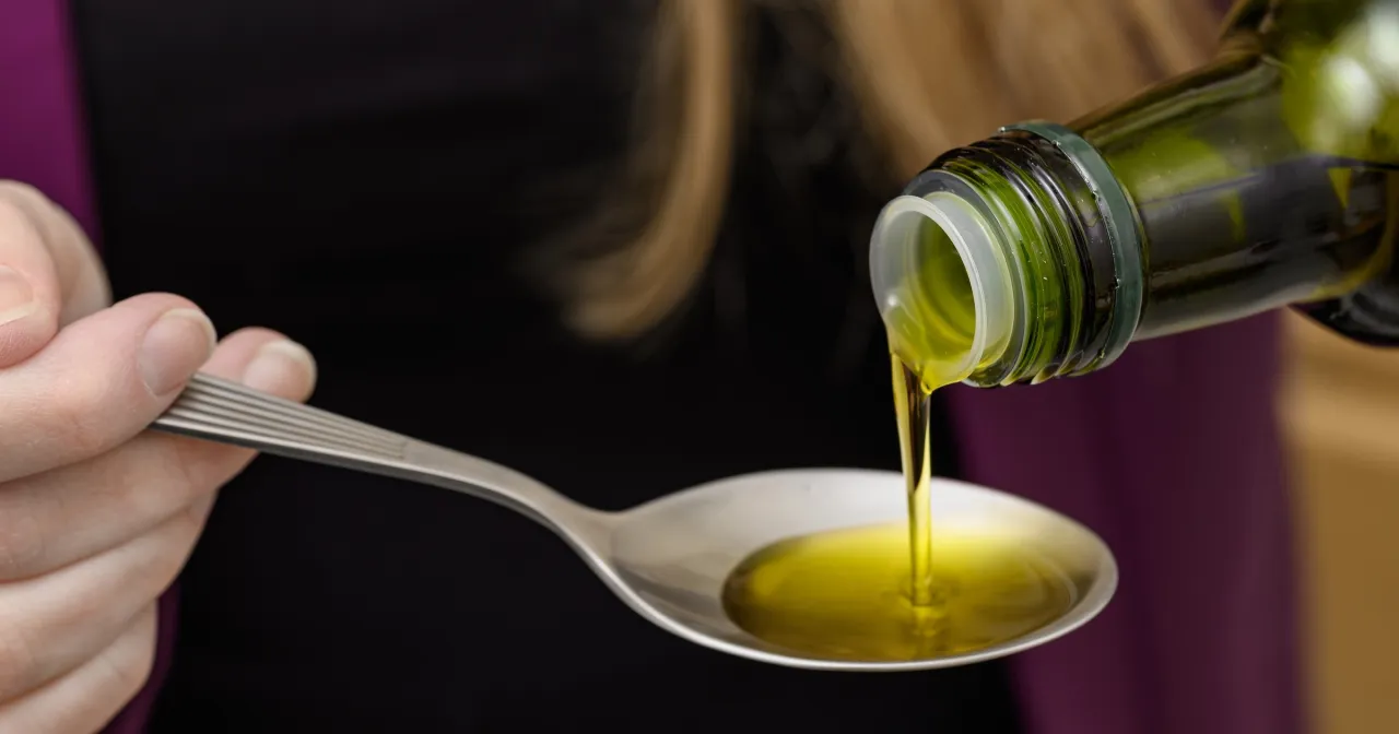 Olej z ostropestu plamistego wylewa się z zielonej butelki na łyżkę.