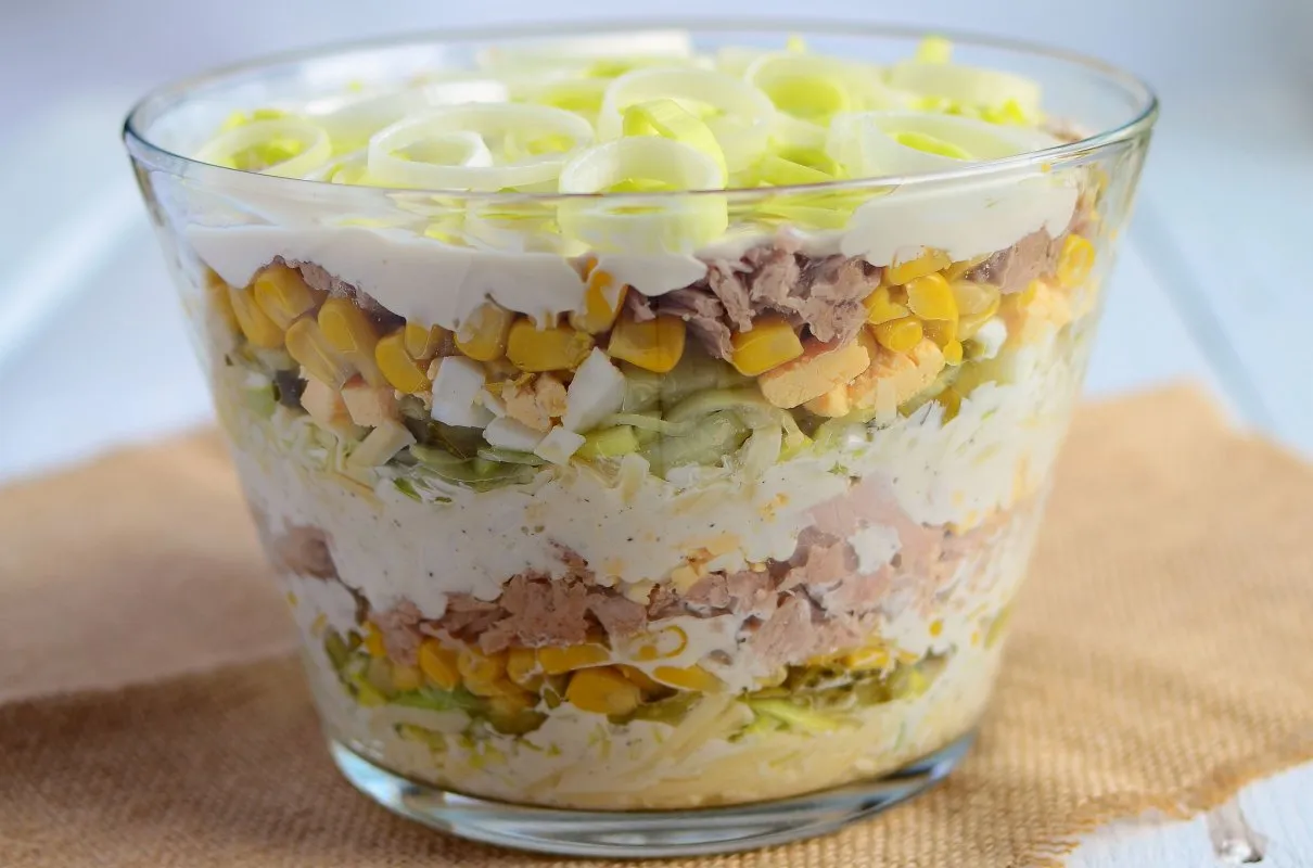 Warstwowa sałatka z tuńczyka, kukurydzy, jajek i pora w szklanej misie. Idealna inspiracja, jak zrobić sałatkę z tuńczyka.