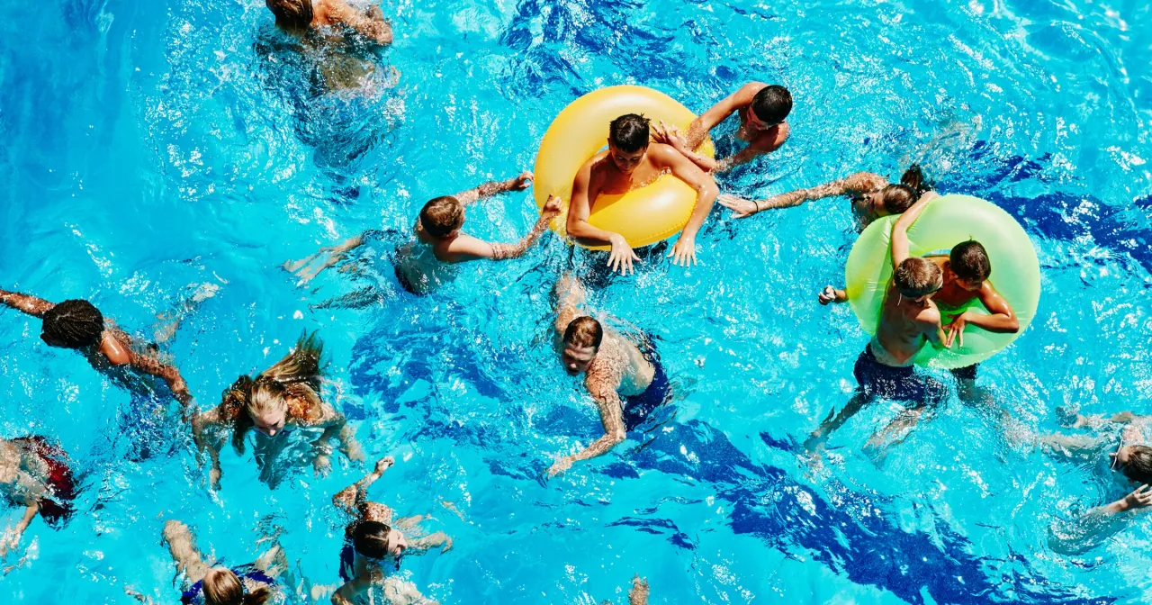 Dzieci bawią się w basenie, niekt&oacute;re z nich mają koła do pływania, jakby miały ogon syreny do pływania.